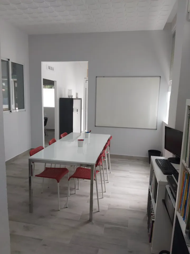 Aula con mesa blanca, sillas rojas y pizarra